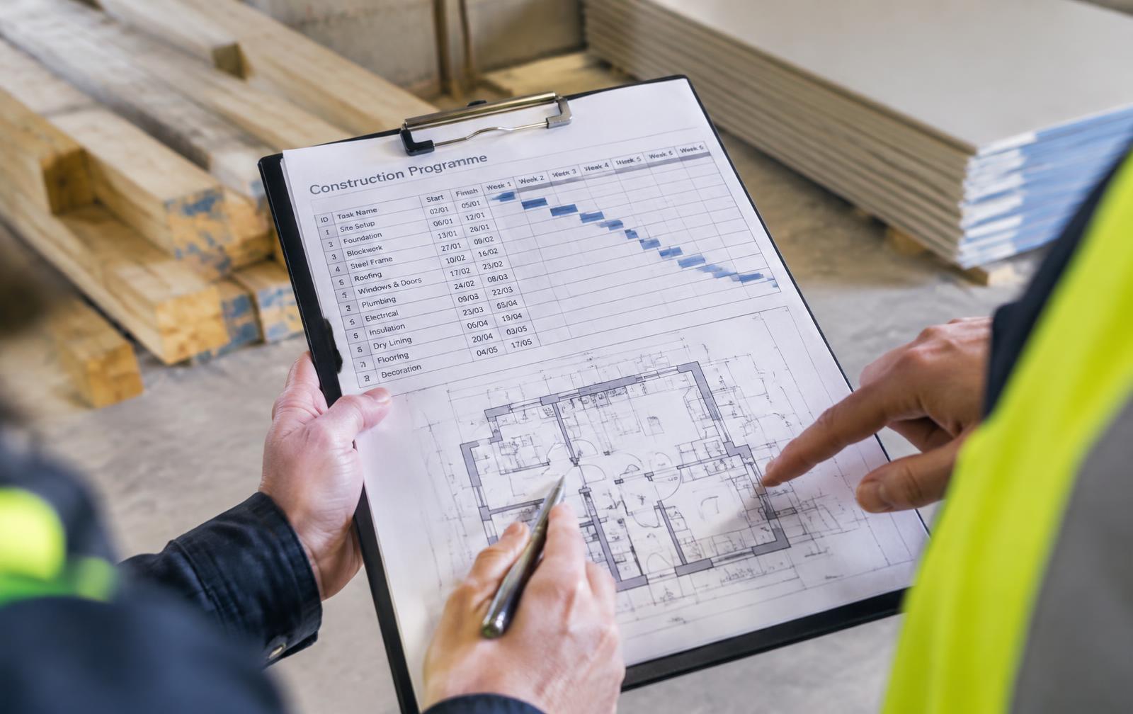 Hands reviewing a construction programme and floor plan on site
